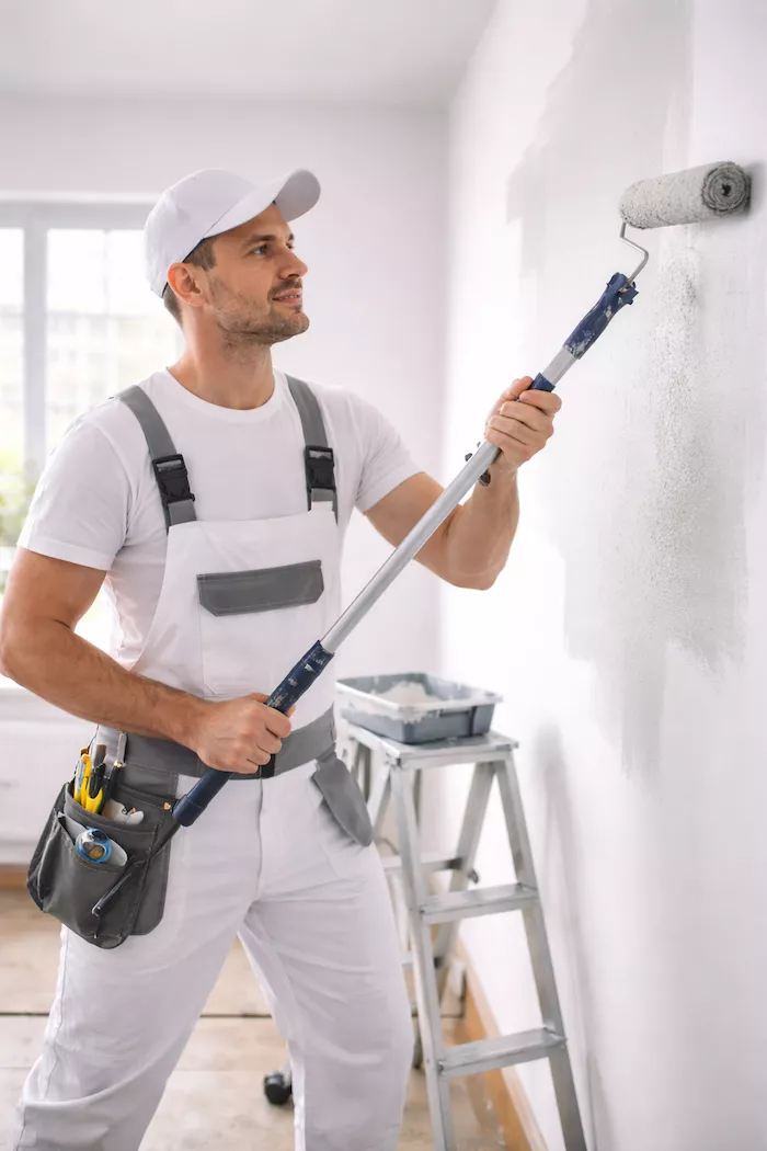 Professionell målare som utför måleriarbete inomhus – noggrant arbete med roller och verktygsbälte i ljus bostadsmiljö.